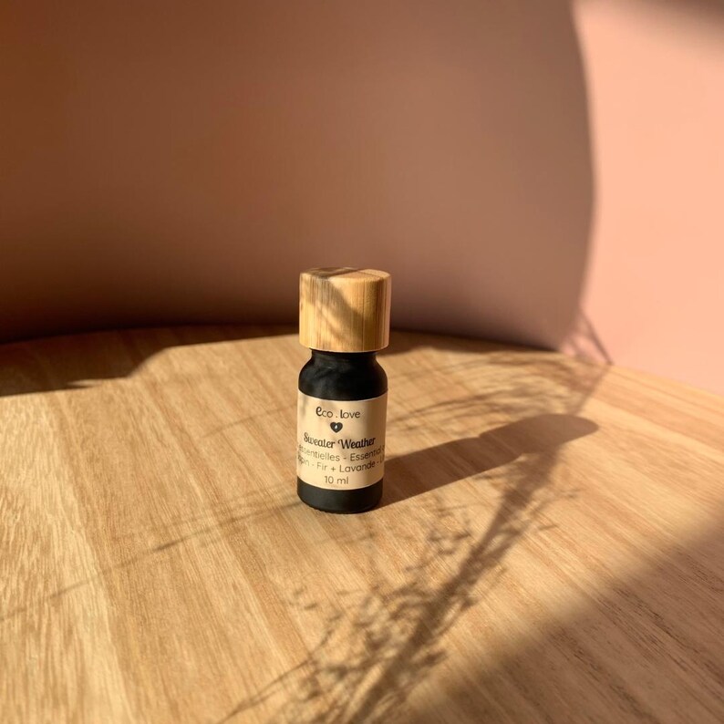 May include: A small, black glass bottle with a wooden cap. The bottle is labeled "Eco Love" and "Sweater Weather" with a heart symbol. The bottle contains essential oils and is 10 ml.