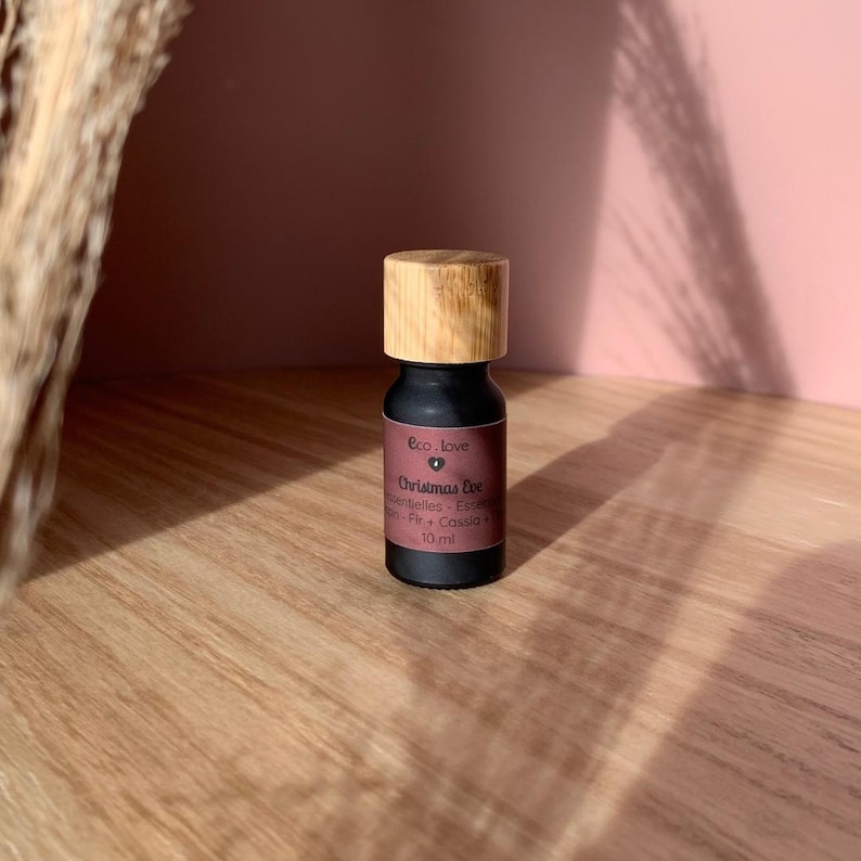 May include: A small, black glass bottle with a wooden cap. The bottle is labeled "Eco. Love Christmas Eve" and contains essential oils. The bottle is sitting on a wooden surface.