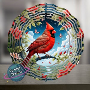 May include: A metal wind spinner with a red cardinal perched on a branch. The cardinal is surrounded by red flowers and butterflies against a blue sky with clouds. The wind spinner has multiple layers of metal that spin in the wind.