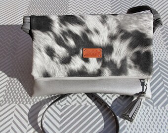 May include: A black and white cowhide print crossbody bag with a silver zipper and a tassel. The bag has a brown leather tag with the text "Made in Italy" on it.