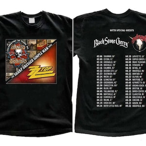 May include: Black t-shirt with a graphic of a skull and crossbones with the text "Celebrating 50 Years of The Sharp Dressed Simple Man Tour" and the band name "ZZ Top" in yellow and red letters. The back of the shirt lists tour dates with the text "With Special Guests Black Stone Cherry" and the band name "Dutchess" in white letters.