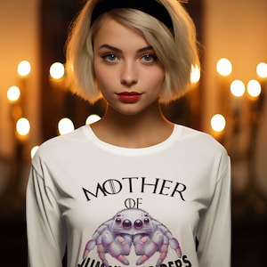 May include: White long-sleeved shirt with a black and white graphic of a spider and the text "Mother of Jumping Spiders".
