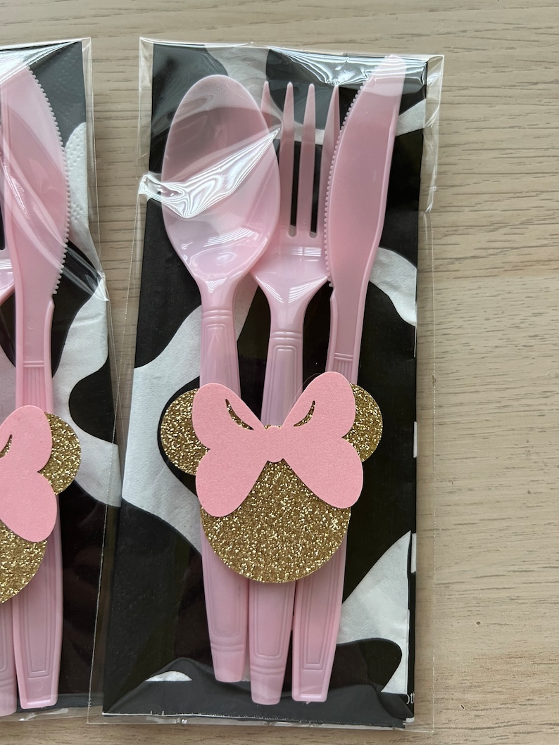 Puede incluir: Juego de cubiertos de pl&aacute;stico rosa con un dise&ntilde;o de Minnie Mouse con lazo rosa y purpurina dorada. El juego incluye un tenedor, un cuchillo y una cuchara.