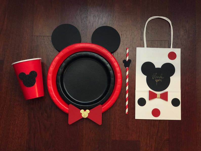 Puede incluir: Un conjunto de art&iacute;culos para fiestas con tem&aacute;tica de Mickey Mouse. Incluye una taza roja, platos y una bolsa de regalo con pajarita y la frase "gracias". El conjunto tambi&eacute;n tiene una pajita y orejas de rat&oacute;n negras.