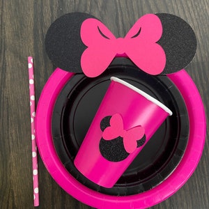 Puede incluir: Suministros para fiestas de Minnie Mouse en rosa y negro, que incluyen un vaso de papel, un plato de papel y una pajita con lunares blancos.