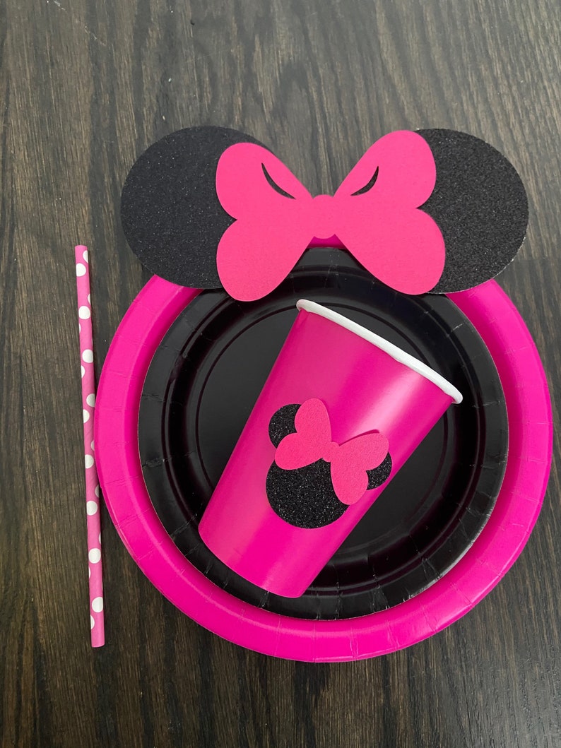 Puede incluir: Suministros para fiestas de Minnie Mouse en rosa y negro, que incluyen un vaso de papel, un plato de papel y una pajita con lunares blancos.