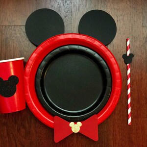 Puede incluir: Un juego de fiesta con tem&aacute;tica de Mickey Mouse, que incluye una taza y platos rojos con una silueta negra. Tambi&eacute;n incluye una pajita a rayas rojas y blancas, orejas negras y una pajarita roja con centro dorado. Ideal para una fiesta tem&aacute;tica.