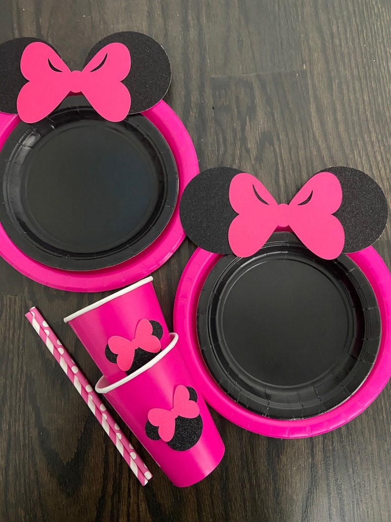 Puede incluir: Platos y vasos de papel rosa y negro con un dise&ntilde;o de Minnie Mouse. Los platos tienen un centro negro y un borde rosa. Los vasos tienen una base rosa y una cabeza de Minnie Mouse negra con un lazo rosa en la parte superior.