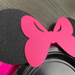 Puede incluir: Orejas de Minnie Mouse de fieltro negro y rosa con un gran lazo rosa. Las orejas est&aacute;n hechas de fieltro negro con una textura brillante. El lazo est&aacute; hecho de fieltro rosa y tiene un dise&ntilde;o simple.