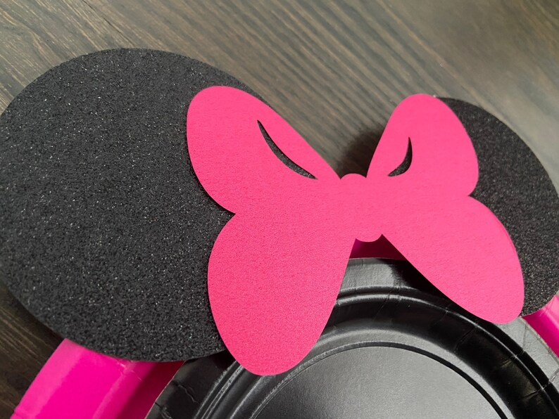 Puede incluir: Orejas de Minnie Mouse de fieltro negro y rosa con un gran lazo rosa. Las orejas est&aacute;n hechas de fieltro negro con una textura brillante. El lazo est&aacute; hecho de fieltro rosa y tiene un dise&ntilde;o simple.