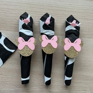 Puede incluir: Tres servilletas de papel con estampado de cebra en blanco y negro con anillos de servilleta de lazo rosa y dorado. Los anillos de lazo tienen un acabado brillante.