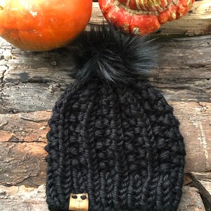 May include: Black knitted beanie with a fluffy pom pom and a brown leather tag that says "Hope & Stitches".