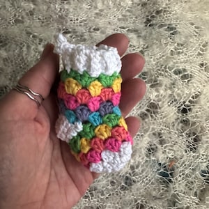 May include: A small, colorful crocheted stocking with a white cuff. The stocking is made with a variety of colors, including pink, yellow, green, and blue.