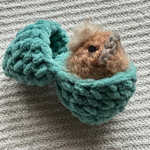 Op de afbeelding: Een tealblauw gehäkeld vogelnest met een bruin en wit gehäkelde vogel erin.