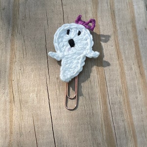 May include: White crocheted ghost with a purple bow, attached to a copper paper clip.