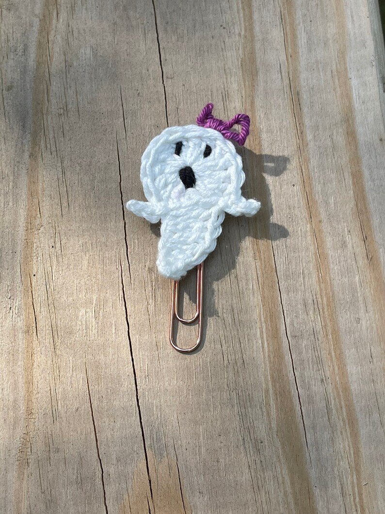 May include: White crocheted ghost with a purple bow, attached to a copper paper clip.