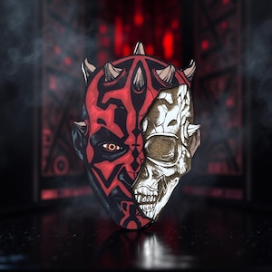 May include: A half-face mask featuring a split design: one side depicts a red and black character with horns, the other a skull. The mask has a detailed, artistic style, with a dark background and red accents.