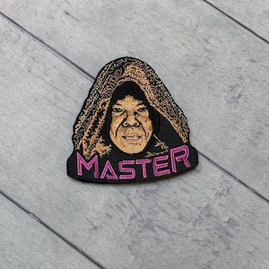 Puede incluir: Un parche bordado con una persona con una túnica marrón con capucha y la palabra "MASTER" en letras rosas.