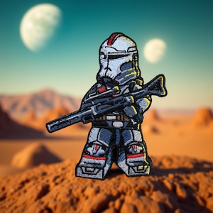 May include: Embroidered patch depicting a futuristic soldier in blue, grey, and red armour, holding a rifle. The patch has yellow detailing. The background shows a desert landscape with two moons in the sky.