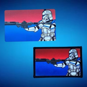 Könnte beinhalten: Zwei rechteckige Aufnäher mit einem weiß-blauen gepanzerten Soldaten, der ein Blastergewehr anvisiert. Der Hintergrund verläuft von Rot zu Blau. Ein Aufnäher hat einen schwarzen Rand.