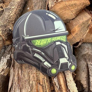 Op de afbeelding: Een zwarte en groene helm met een vizier en de tekst "Death to Rebels" erop. De helm heeft een gedetailleerd ontwerp met een textuur.