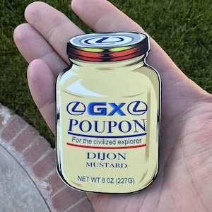 Könnte beinhalten: Ein Aufkleber in Form eines Dijon-Senfglases. Das Etikett lautet "GXO Poupon" mit dem Text "For the civilized explorer" und "Dijon Mustard". Der Aufkleber ist gelb mit blauen und roten Akzenten und trägt die Aufschrift "NET WT 227g".