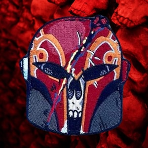May include: A red, blue, and orange embroidered patch of a skull wearing a helmet. The helmet has a cracked design and a lightning bolt running through it.