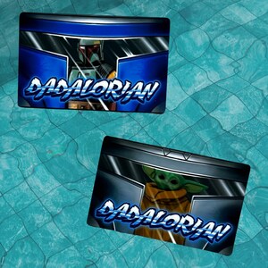 May include: Two blue and black rectangular signs with the text "DADALORIAN" in a blue and white stylized font. The top sign features a Star Wars character, Boba Fett, in a blue and black helmet. The bottom sign features a Star Wars character, Grogu, in a blue and black helmet.