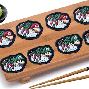 May include: A wooden sushi serving tray with seven colorful sushi pieces featuring Mario and Luigi characters. The tray has a small wooden stand and comes with a pair of wooden chopsticks.