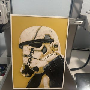 Peut inclure: Un gros plan sur un casque de Stormtrooper de Star Wars blanc et noir sur un fond jaune. Le casque est usé et a un aspect vieilli.