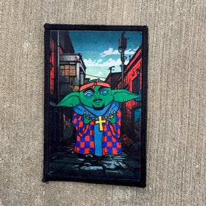 May include: A green and blue cartoon character with a gold cross necklace and a red and blue checkered shirt, standing in an alleyway. The character has a black bandana on its head and is wearing gold earrings.