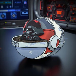 Op de afbeelding: Een cartoon-stijl Darth Vader-figuur in een pod-achtig voertuig. Het voertuig is voornamelijk blauw, rood en wit, met een cirkelvormig ontwerp. De Darth Vader-figuur is zwart met een rode accent op de helm. De achtergrond is een vage interieur.
