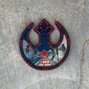 Op de afbeelding: Een cirkelvormig wandobject met het symbool van de Rebel Alliance in zwart met rode accenten. Het midden toont een TIE fighter-afbeelding tegen een ruimteachtergrond met de tekst I HAVE YOU NOW! in een vetgedrukt, stripboekachtig lettertype onderaan.