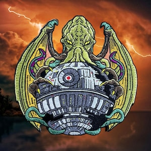 May include: A green and yellow embroidered patch depicting a tentacled creature with wings, holding a round, gray object with a red circle in the center.