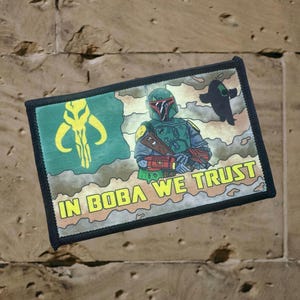 May include: A green, black, and yellow embroidered patch with a Star Wars character, Boba Fett, and the text "In Boba We Trust".