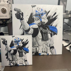 May include: Two different sized prints of a Star Wars clone trooper with blue markings and a blaster rifle. The background is a white canvas with black brushstrokes.