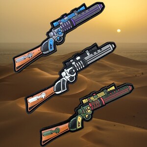 May include: Three different colored toy blaster guns with a desert background. The blasters are all in a similar style with a scope and a barrel. The colors are purple, black and white, and orange and green.