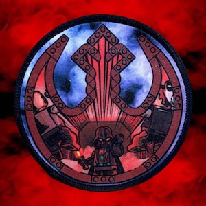 May include: A round, embroidered patch featuring a dark blue and red Rebel Alliance symbol with a Lego Darth Vader figure in the center. The patch has a black border.