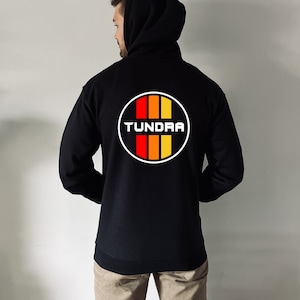 May include: Black hooded sweatshirt with a white circle graphic on the back. The graphic features a red, orange, and yellow striped design with the word "TUNDRA" in white text.