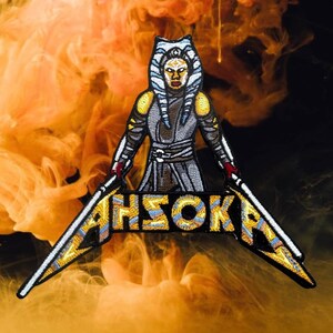 Pode incluir: Um remendo bordado com Ahsoka Tano de Star Wars. O remendo é amarelo, azul e branco com contorno preto. O texto "Ahsoka" está em um design de banda metálica.