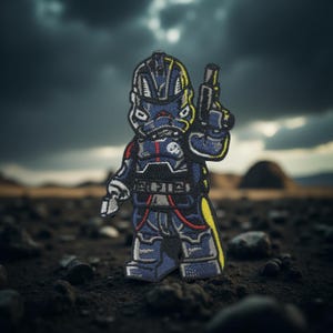 May include: Embroidered patch featuring a stylized soldier figure in a dark blue uniform with yellow and red accents. The figure is holding a gun and has a skull emblem. The patch is set against a blurred outdoor background.