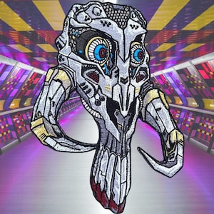 May include: A silver, white, and gold embroidered patch of a stylized skull with horns and glowing blue eyes. The skull is detailed with intricate patterns and textures.