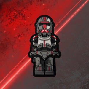 Może przedstawiać: Klonowy żołnierz z kreskówki w kolorze czerwonym i szarym, z białym hełmem i czerwoną osłoną twarzy. Żołnierz trzyma karabin blaster w prawej ręce.