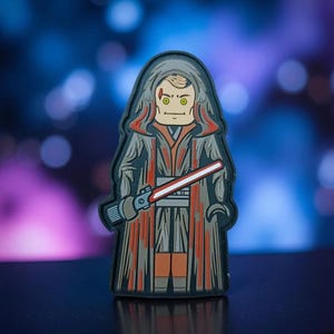 May include: A stylized pin featuring a hooded figure with a red lightsaber. The figure is dressed in a dark gray robe with red and orange accents. The background is a blurred mix of blue, purple, and white.