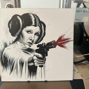 May include: A black and white illustration of a woman holding a gun with a red blast coming out of the barrel. The woman is wearing a white shirt and has a serious expression on her face.