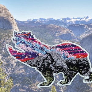 May include: A black bear silhouette embroidered patch with a colorful American flag design. The patch features a mountain range in the background.