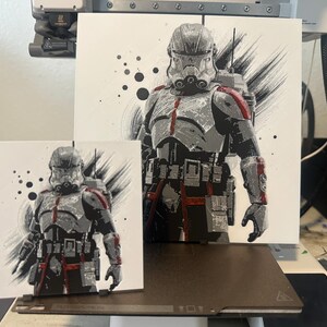 May include: A black and white illustration of a Star Wars clone trooper with red accents. The trooper is wearing a helmet and has a blaster rifle. The background is a white canvas with black splatters.