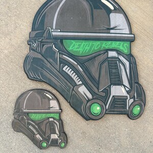 Op de afbeelding: Twee zwart-groene illustraties van een Star Wars Stormtrooper-helm met de tekst "Death to Rebels" op het vizier.