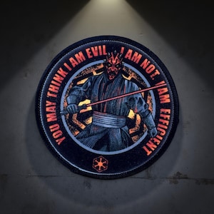 May include: A black and red circular patch with a Star Wars character, Darth Maul, holding a red lightsaber. The text on the patch reads "You may think I am evil. I am not. I am efficient."