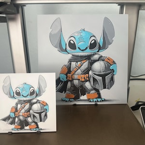 May include: Two framed illustrations of a blue Stitch character from the Disney movie Lilo & Stitch dressed as a Mandalorian from the Star Wars series. The larger illustration shows Stitch holding a Mandalorian helmet. The smaller illustration shows Stitch holding a Mandalorian helmet and standing on a black stand.